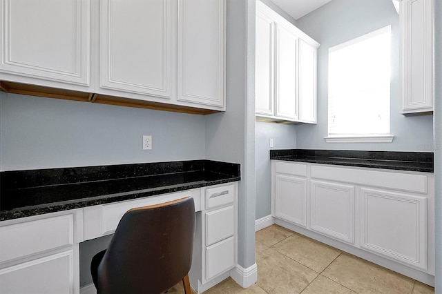 kitchen featuring dark stone counters, built in desk, light tile patterned flooring, and white cabinets