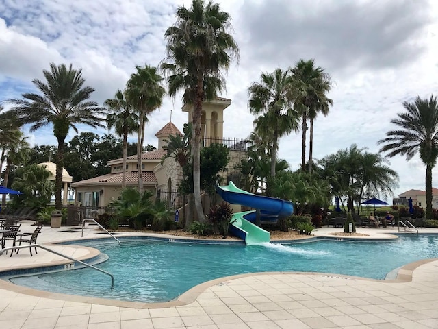 pool with fence, a water slide, and a patio