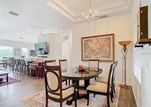 dining space with hardwood / wood-style floors, a chandelier, and a tray ceiling