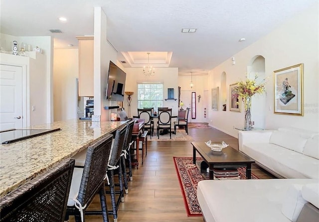 living room featuring an inviting chandelier, dark wood-type flooring, and a raised ceiling