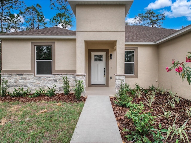 doorway to property featuring a shingled roof, stone siding, and stucco siding