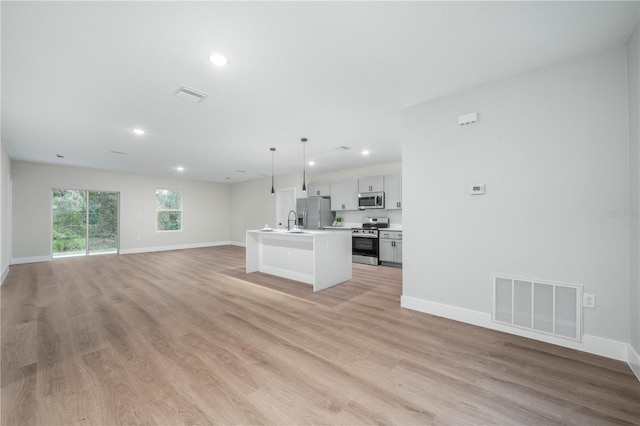 kitchen with visible vents, an island with sink, appliances with stainless steel finishes, open floor plan, and light countertops