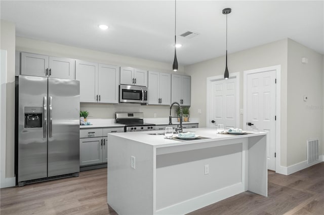 kitchen with visible vents, light countertops, appliances with stainless steel finishes, hanging light fixtures, and an island with sink