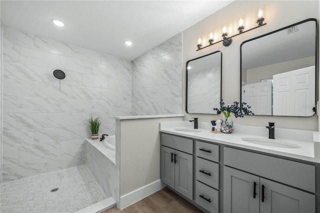 full bathroom featuring a bath, double vanity, a sink, and wood finished floors