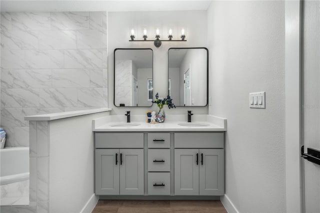 bathroom with double vanity, wood finished floors, a tub with marble appearance, and a sink