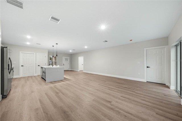 unfurnished living room featuring visible vents, a sink, light wood-style flooring, and baseboards