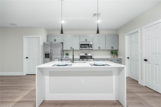 kitchen with a center island with sink, visible vents, appliances with stainless steel finishes, light countertops, and pendant lighting