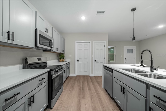 kitchen with gray cabinetry, a sink, light countertops, appliances with stainless steel finishes, and decorative light fixtures