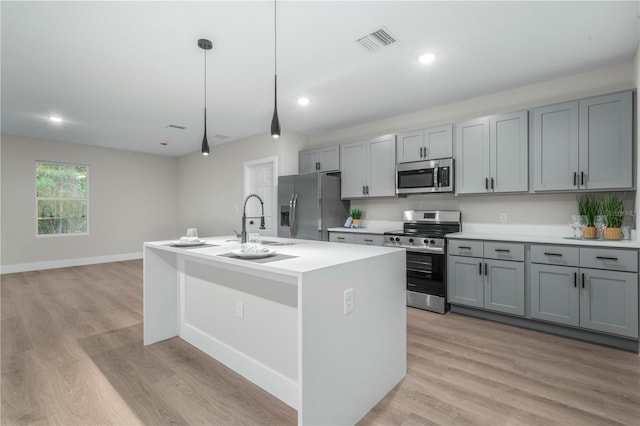 kitchen featuring stainless steel appliances, light countertops, a center island with sink, and visible vents