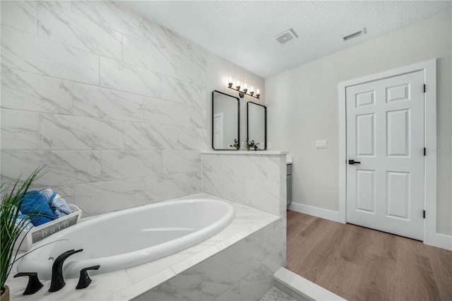 bathroom featuring visible vents, vanity, a textured ceiling, wood finished floors, and a bath