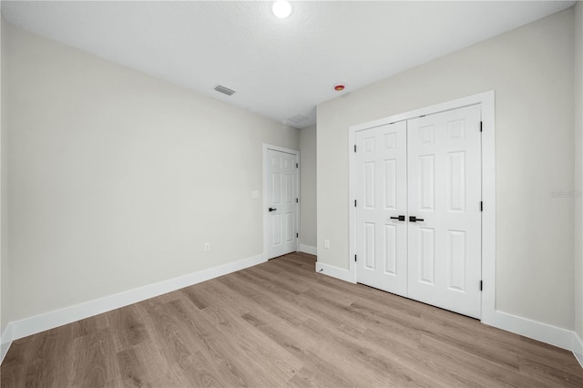 unfurnished bedroom with a closet, light wood-type flooring, visible vents, and baseboards