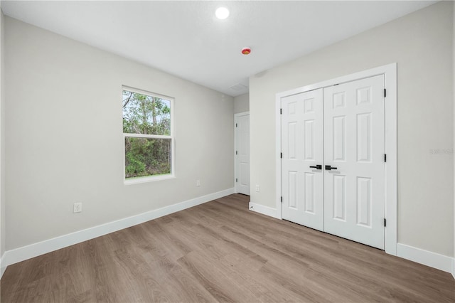 unfurnished bedroom featuring light wood-type flooring, a closet, and baseboards