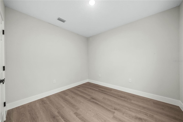 empty room with wood finished floors, visible vents, and baseboards