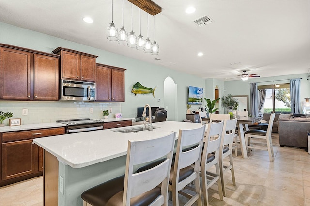 kitchen featuring stainless steel appliances, arched walkways, light countertops, and a center island with sink