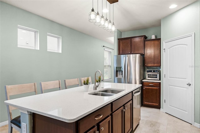 kitchen with an island with sink, appliances with stainless steel finishes, dark brown cabinets, a kitchen bar, and a sink