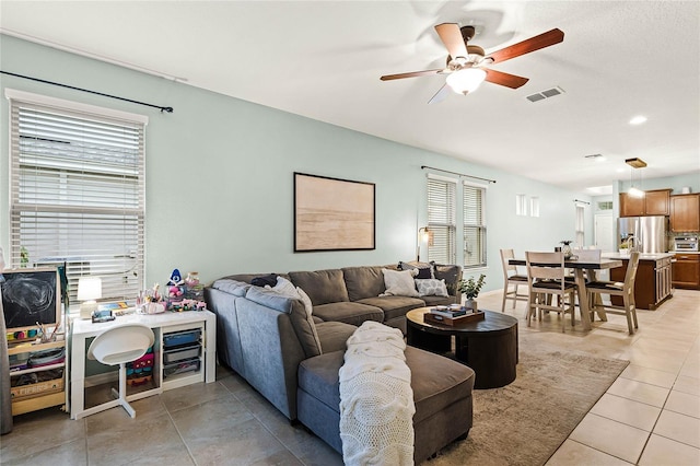 living area with light tile patterned floors, lofted ceiling, visible vents, and a ceiling fan