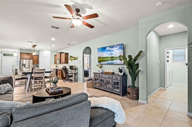 living area featuring arched walkways, ceiling fan, light tile patterned floors, visible vents, and baseboards