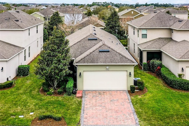 view of front facade featuring an attached garage, decorative driveway, a residential view, stucco siding, and a front yard