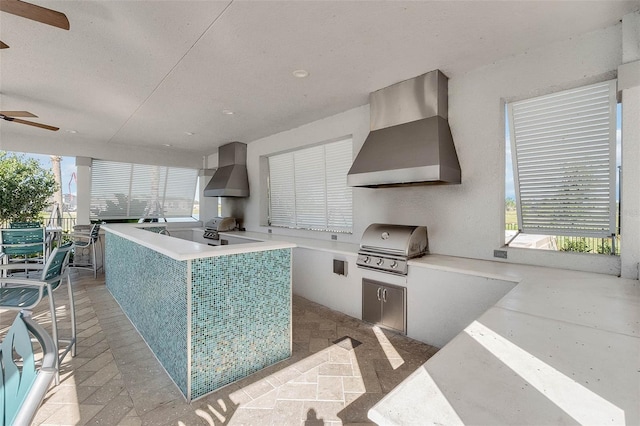 kitchen with wall chimney exhaust hood, light countertops, and a ceiling fan