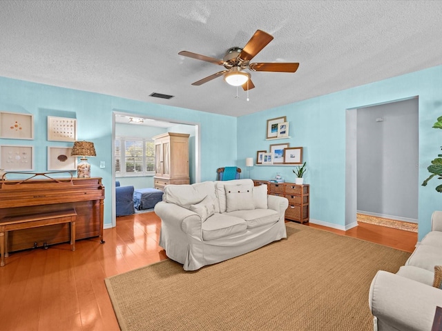 living room featuring hardwood / wood-style floors, ceiling fan, and a textured ceiling