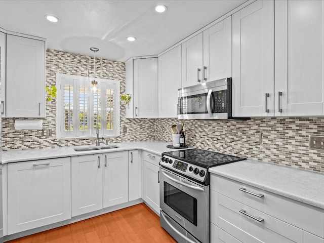 kitchen with appliances with stainless steel finishes, sink, light hardwood / wood-style flooring, decorative light fixtures, and white cabinets