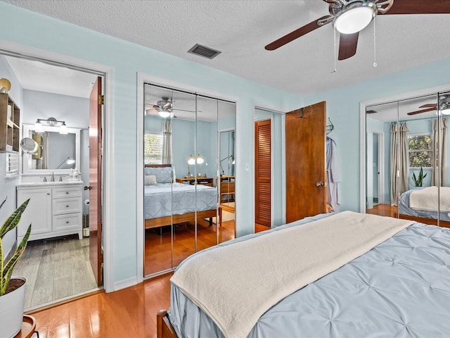 bedroom featuring two closets, light hardwood / wood-style floors, sink, ceiling fan, and a textured ceiling