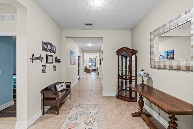 hall with baseboards, visible vents, and a textured ceiling