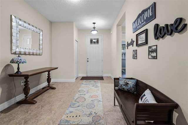 foyer entrance with a textured ceiling, light tile patterned floors, and baseboards
