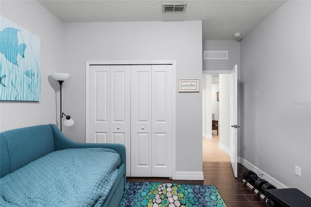 bedroom with a closet, dark wood-style flooring, visible vents, and a textured ceiling
