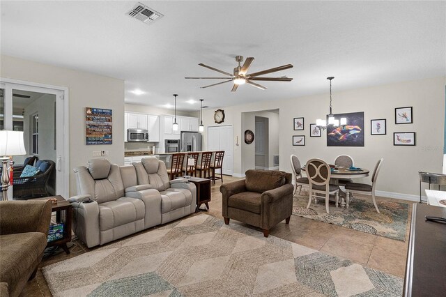living room with ceiling fan with notable chandelier, visible vents, baseboards, and light tile patterned flooring
