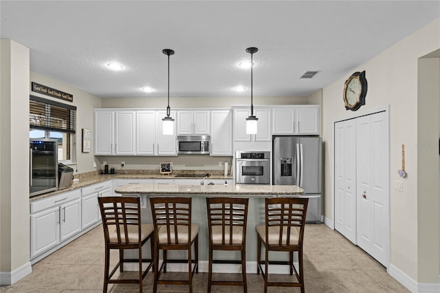 kitchen with visible vents, a kitchen island, light stone countertops, black appliances, and pendant lighting