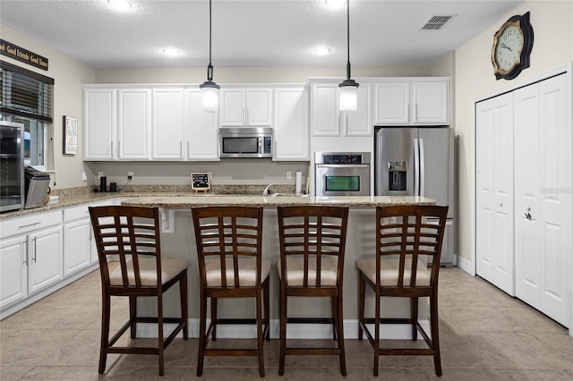 kitchen with white cabinetry, a kitchen breakfast bar, appliances with stainless steel finishes, a center island, and decorative light fixtures