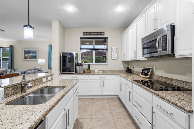 kitchen with stainless steel microwave, open floor plan, black electric cooktop, pendant lighting, and a sink