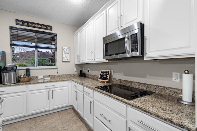 kitchen featuring stone counters, white cabinets, stainless steel microwave, and black electric stovetop