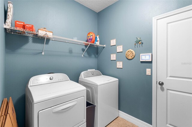 washroom featuring washing machine and clothes dryer, light tile patterned floors, a textured ceiling, laundry area, and baseboards