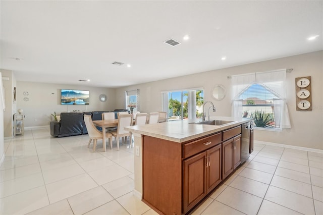 kitchen with a center island with sink, visible vents, brown cabinetry, a sink, and light tile patterned flooring