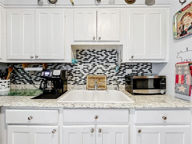 kitchen featuring white cabinets, sink, light stone counters, and decorative backsplash