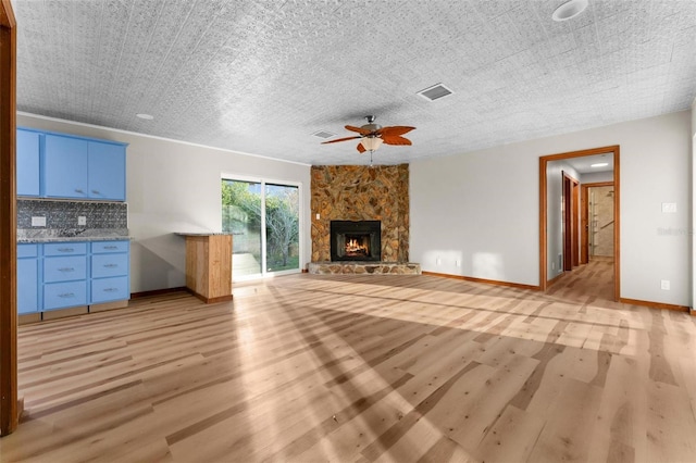 unfurnished living room with ceiling fan, a stone fireplace, visible vents, baseboards, and light wood-style floors