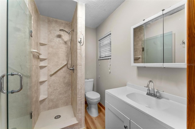 bathroom with toilet, wood finished floors, a textured ceiling, vanity, and a shower stall