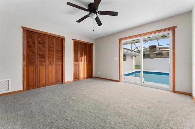 unfurnished bedroom featuring visible vents, baseboards, access to outside, carpet, and two closets