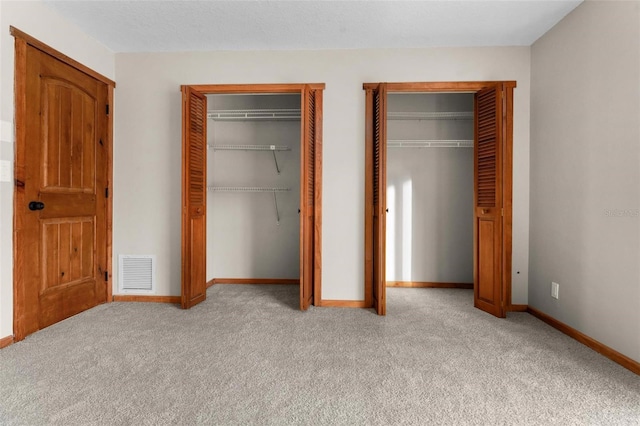 unfurnished bedroom with baseboards, light colored carpet, visible vents, and multiple closets