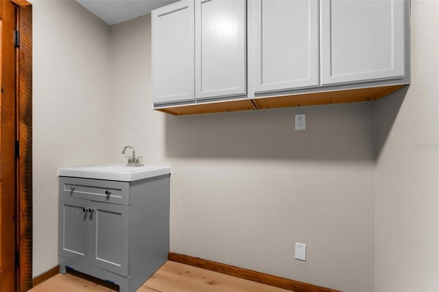 washroom featuring light wood-type flooring, a sink, and baseboards