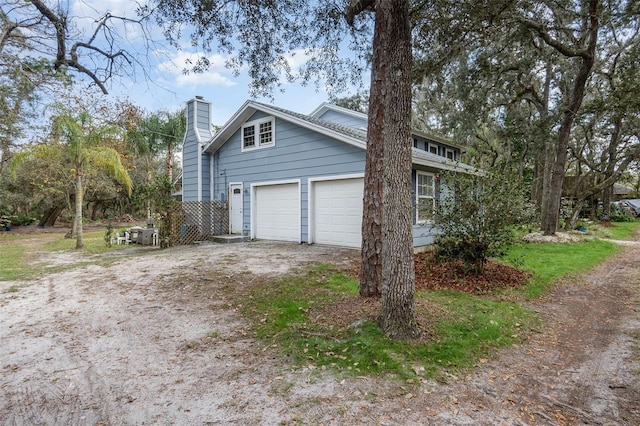 view of home's exterior featuring dirt driveway, a chimney, and a garage