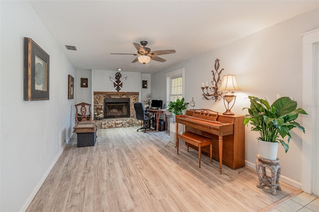 living area with a stone fireplace, a ceiling fan, baseboards, visible vents, and light wood-style floors