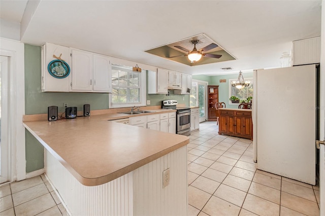 kitchen featuring light tile patterned floors, a peninsula, electric range, freestanding refrigerator, and a tray ceiling