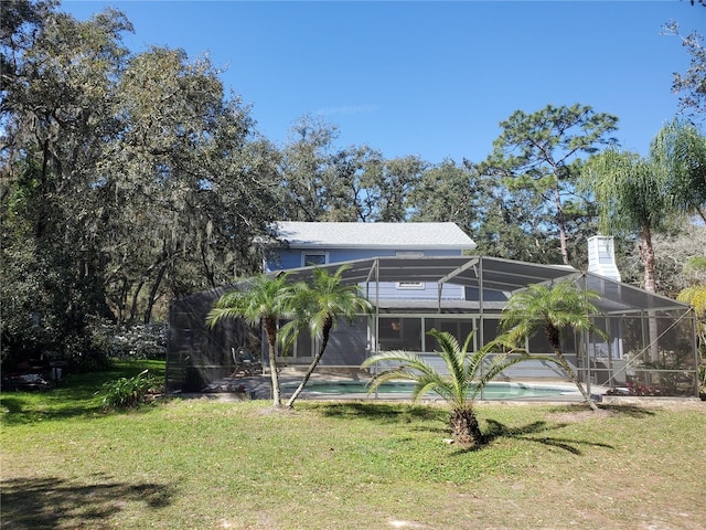 back of property featuring a lanai, a chimney, an outdoor pool, and a yard