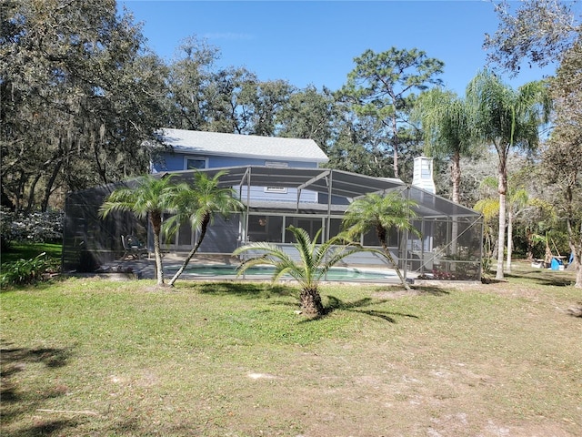 back of house featuring an outdoor pool, glass enclosure, a yard, and a chimney