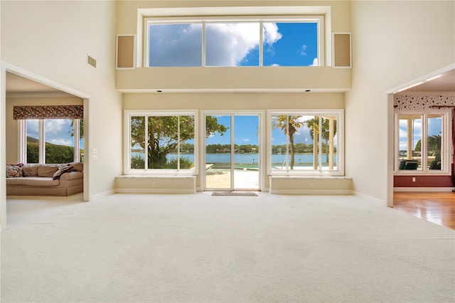 unfurnished living room featuring a water view, baseboards, a high ceiling, and visible vents