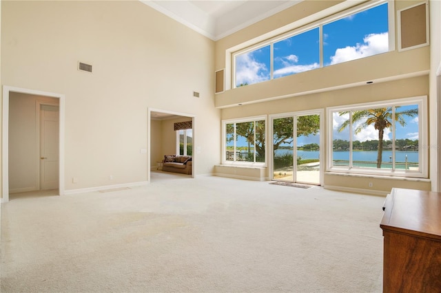 unfurnished living room with baseboards, visible vents, light colored carpet, a water view, and crown molding