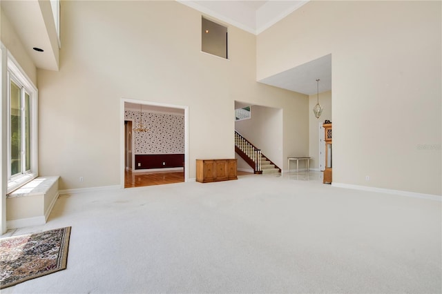 carpeted empty room with a towering ceiling, baseboards, and stairs